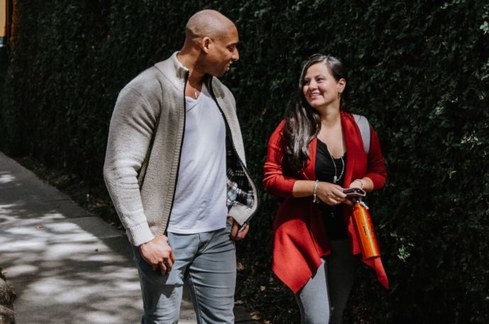 Photos shows two students walking together and smiling while looking at one another.