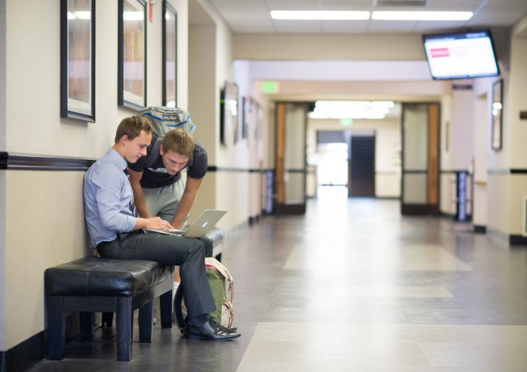 business students look at a laptop in the hallway of Weber Hall