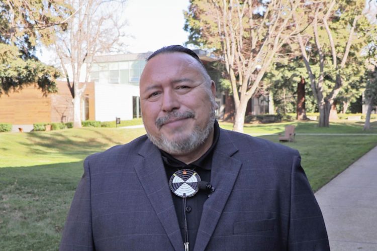 A man in a suit and bolo tie stands outside of the library building 