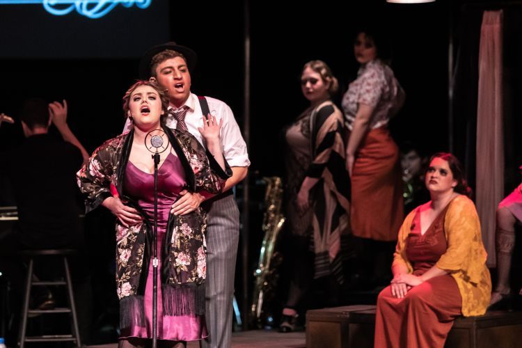 students stand next to a microphone while singing during an opera production