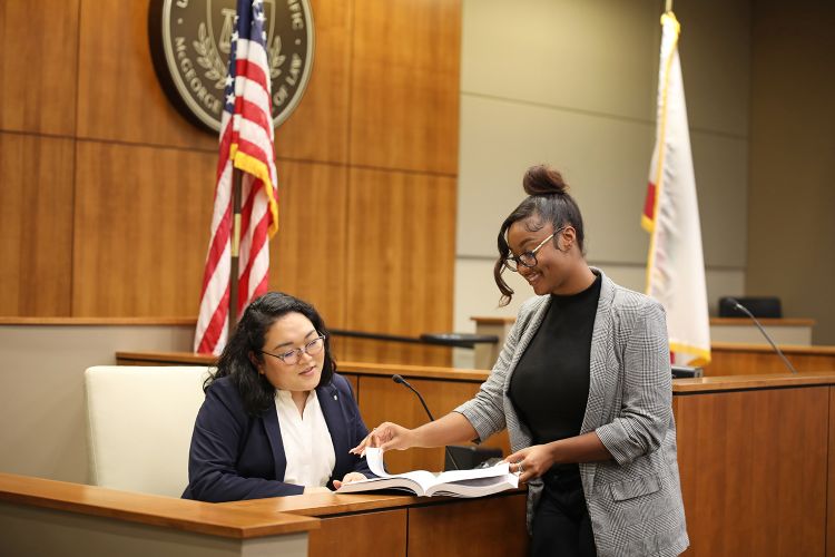 Two students look at a book together in the courtroom