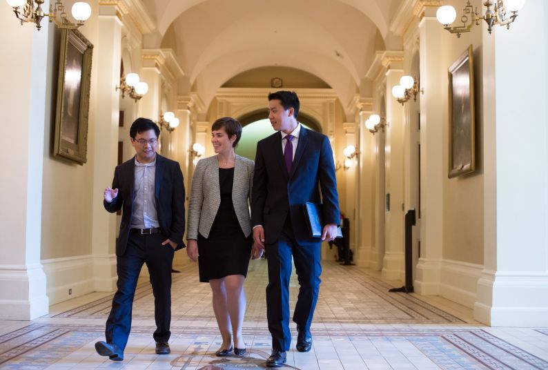 Three students dressed in suits walk through a hallway of the California State Capitol.