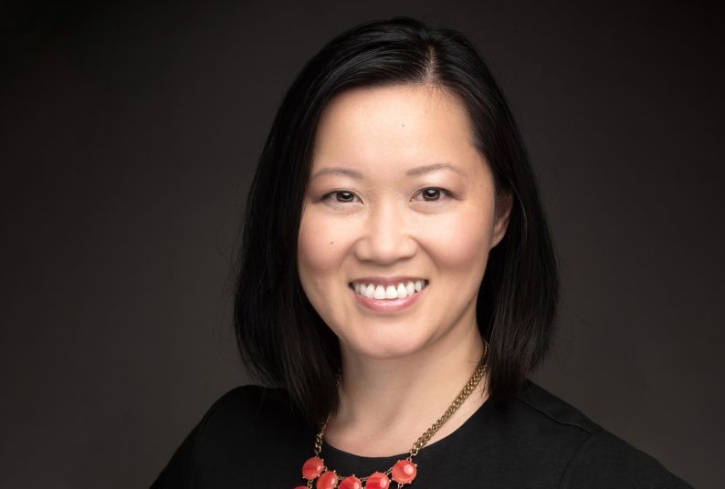 A headshot of an Asian woman in a black shirt, in front of a neutral background 