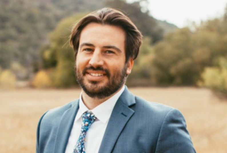 A man wearing a suit smiles for a photo outdoors