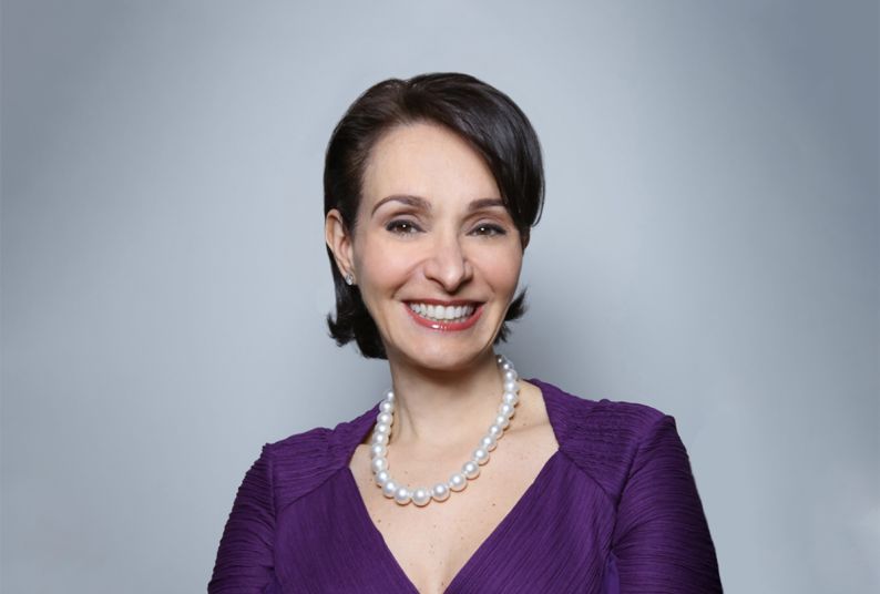 A smiling woman in a purple dress poses with her arms crossed.