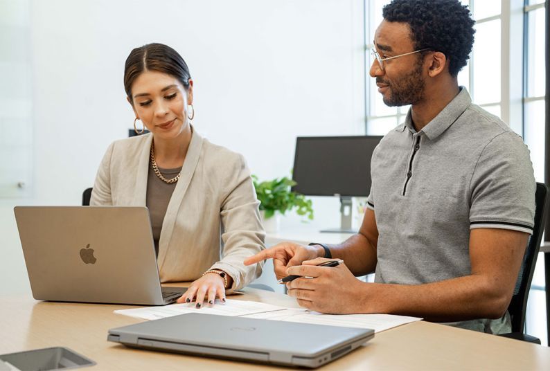 Two people sit at a desk looking at a computer together