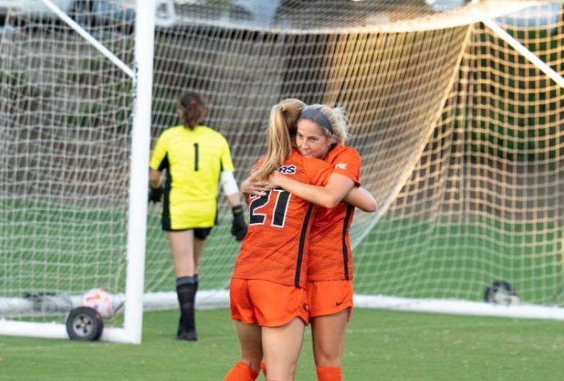 two soccer players hug while standing on the field