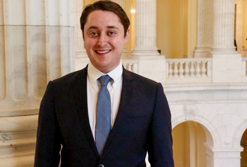 Man in black suit, blue tie, and white under shirt smiles for a headshot.