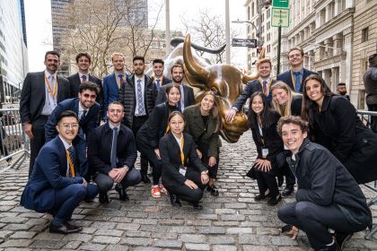 students stand next to the bull of Wall Street statue