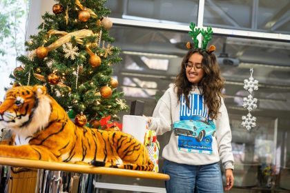 a student stands next to a Christmas tree with a toy Tiger in front of it