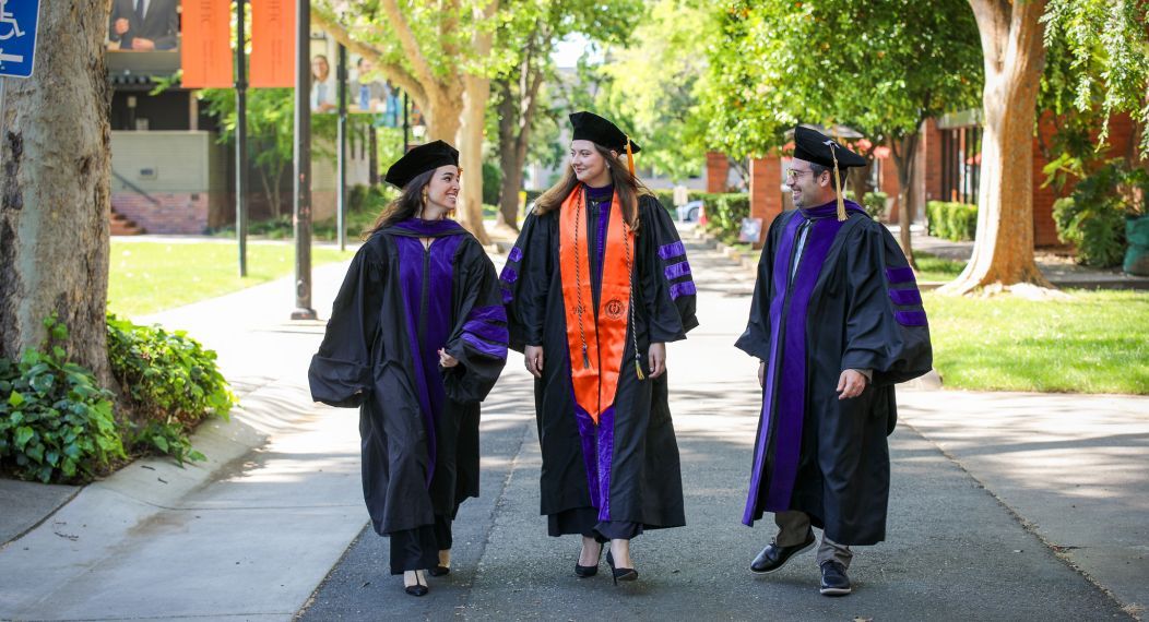 Three graduates walking on campus.